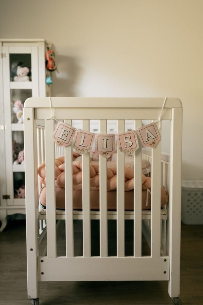 A warmly lit baby nursery featuring a baby crib with a decorative 'Elisa' banner and plush toys.