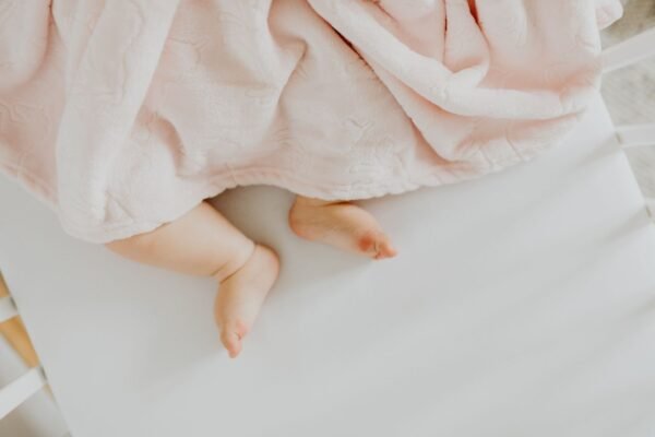 Adorable baby feet peeking out from under a soft pink blanket.