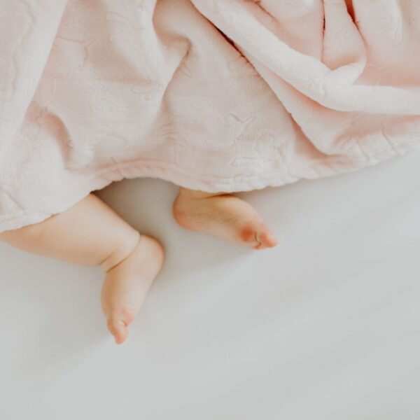 Adorable baby feet peeking out from under a soft pink blanket.