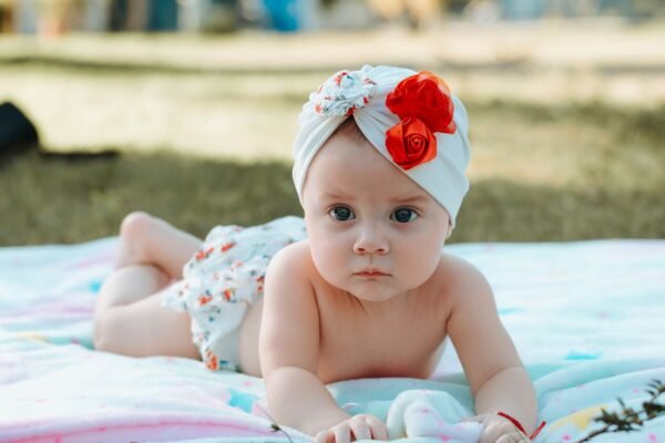 Cute baby in a floral turban lying on a blanket outdoors.