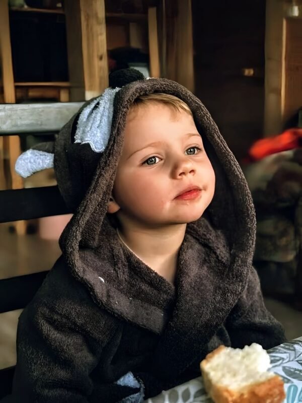 pexels-photo-38950010-38950010 Adorable child in a cozy hooded robe, enjoying a meal at home.
