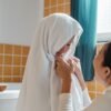Cheerful ethnic mum wiping cute little daughter with big fluffy towel in modern bathroom at home