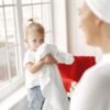 pexels-photo-5523115-5523115 Adorable toddler holding towels by a window with mother nearby, creating a warm family moment.