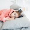 pexels-photo-6202206-6202206 A young girl in a cozy pink robe lying comfortably on a bed with soft pillows.
