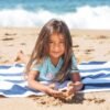 pexels-photo-7849998-7849998 A joyful child lying on a beach towel by the shore, enjoying summer sand.