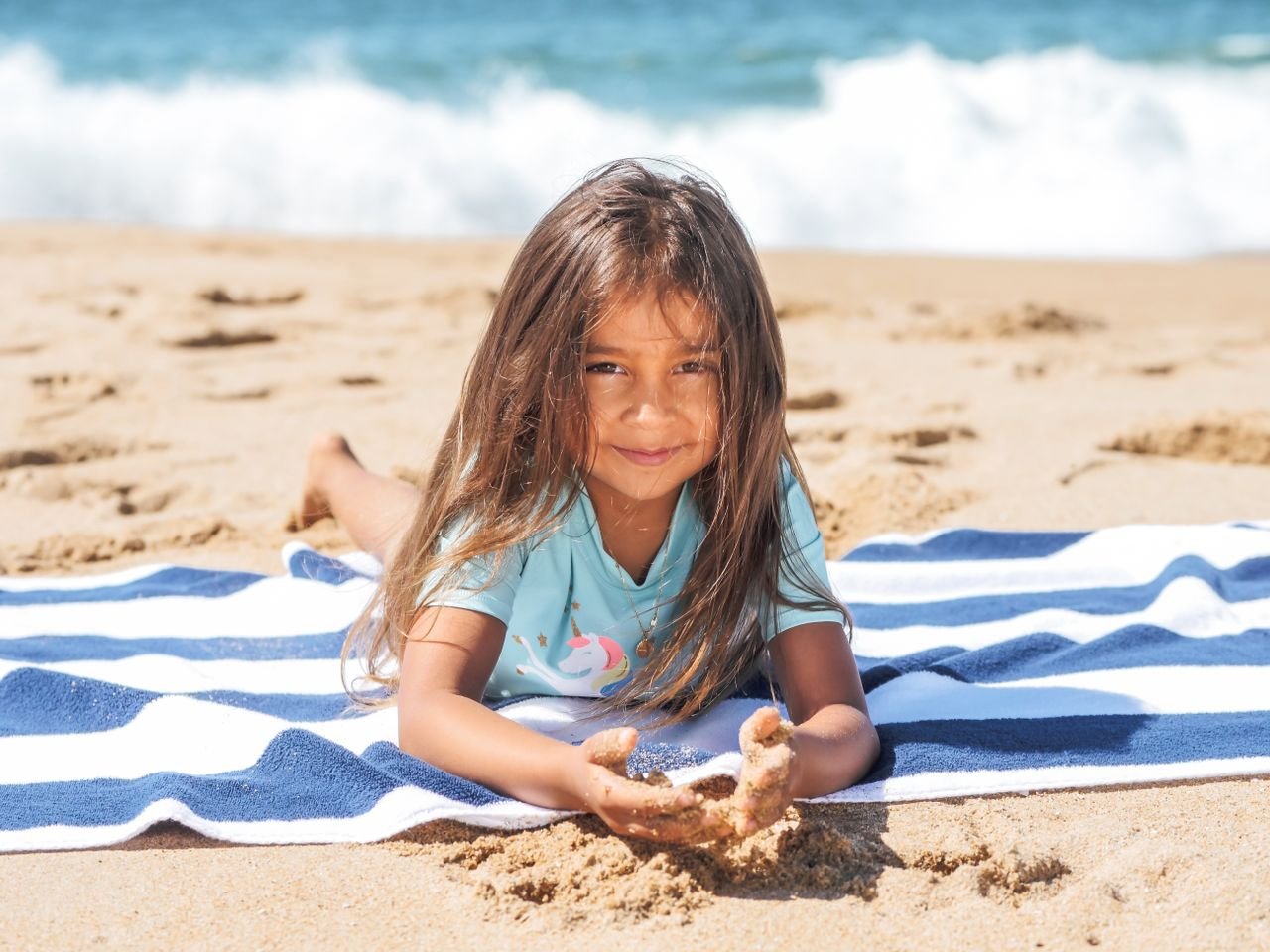 A joyful child lying on a beach towel by the shore, enjoying summer sand.